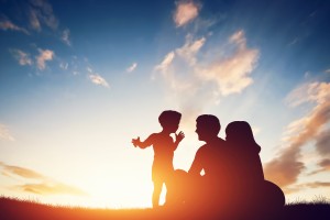 Happy family together, parents with their little child sitting on grass at sunset